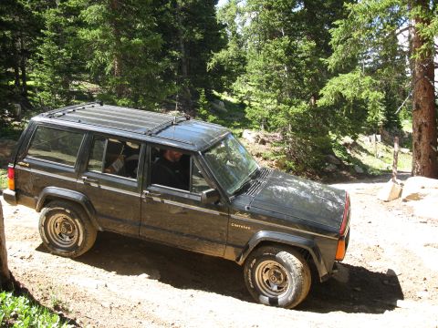 1978 Ford F-150 - A dark green Jeep Cherokee Limited navigates a wooded dirt trail.