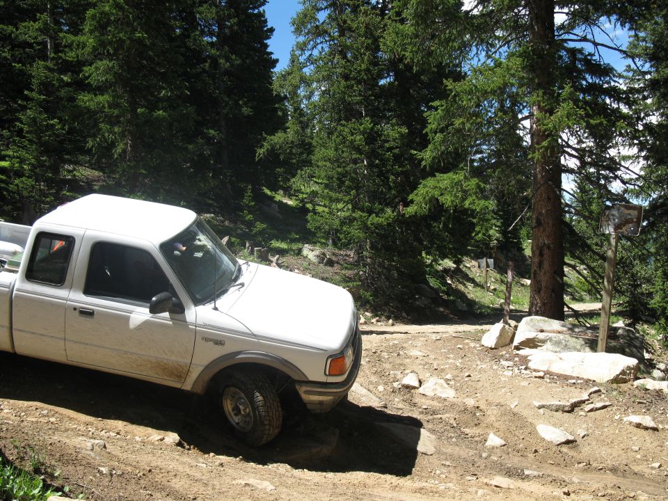 White pickup truck driving on a dirt road in a forest