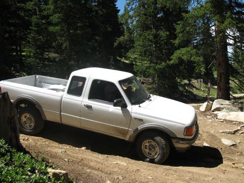 1978 Ford F-150 - A white Ford Ranger pickup truck navigates a dirt road through a forest with rocky terrain.