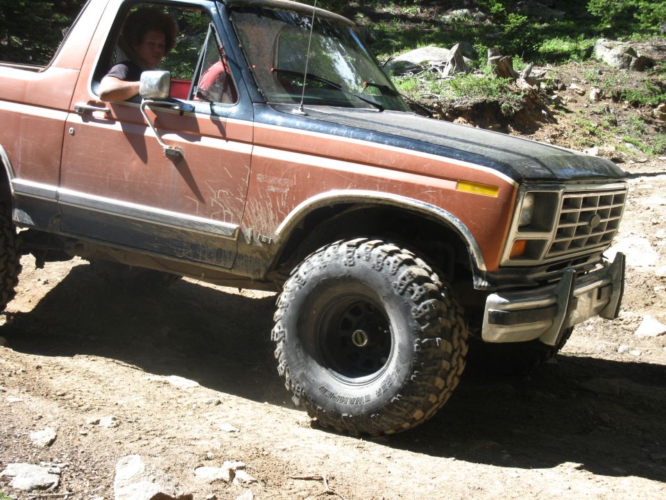 Brown Ford Bronco with black hood and off-road tires on a dirt path