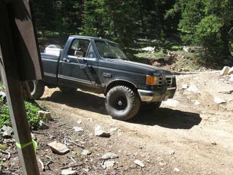 1978 Ford F-150 - This black pickup truck, likely a 1987 model, navigates a rocky dirt road in a wooded area.