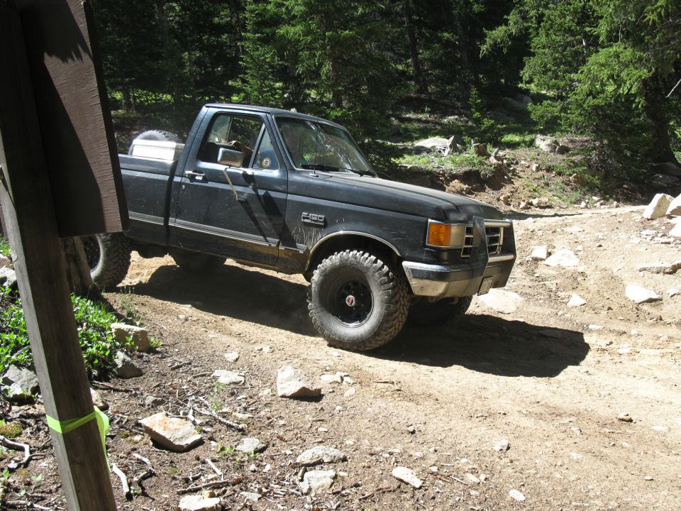 Black pickup truck with off-road tires on a dirt road. Grille indicates 1987 model year