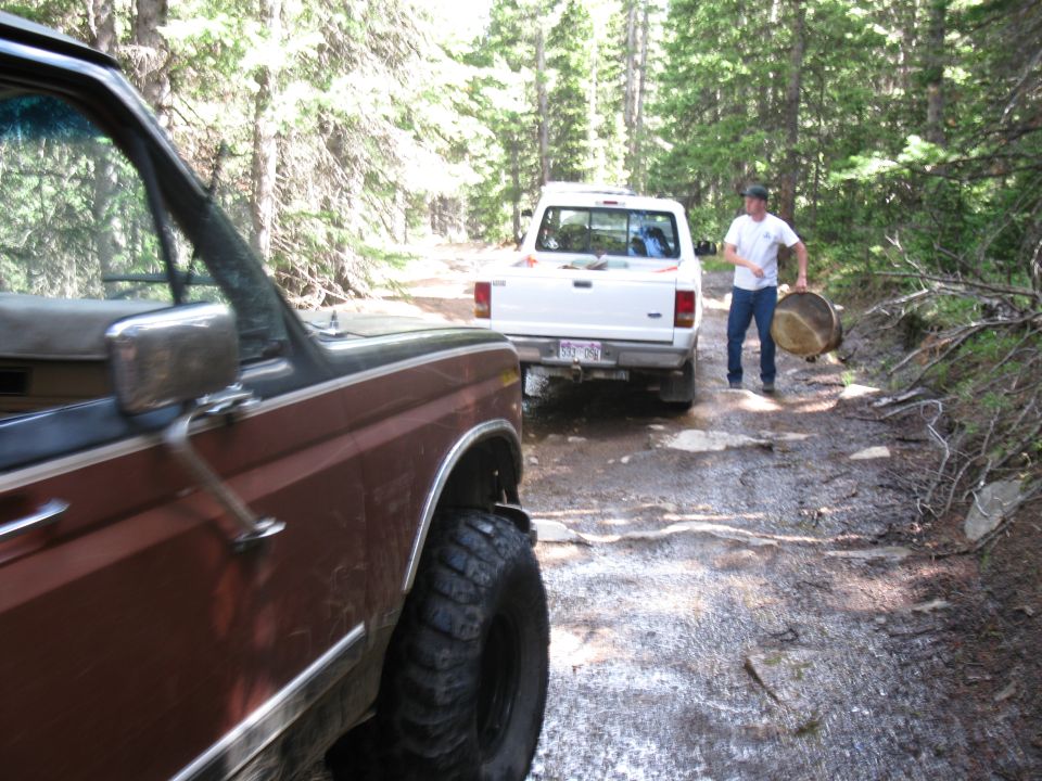 Front of a brown truck, rear of a white truck with a man carrying a large round object