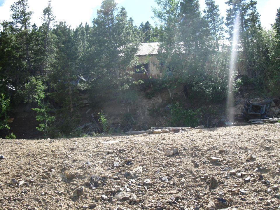 Abandoned building on a hillside surrounded by trees, with a debris-strewn foreground