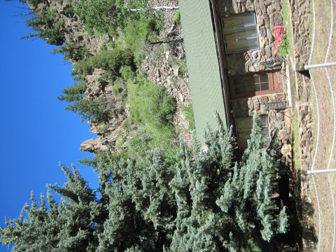 1978 Ford F-150 - A stone building with a green roof is surrounded by trees and rocky terrain under a bright blue sky.