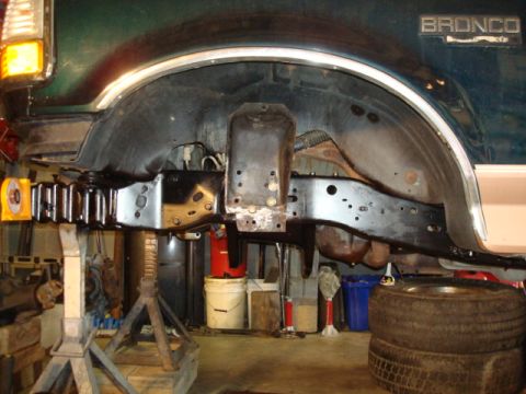 1995 Ford Bronco - The frame of a 1995 Ford Bronco is visible, supported by jack stands in a workshop setting.