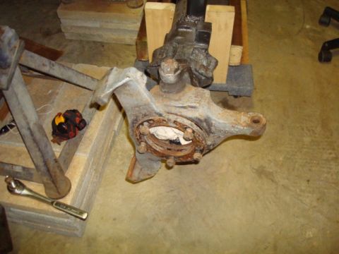 1995 Ford Bronco - A detached vehicle front axle assembly sits on blocks, with a wrench and gloves visible.