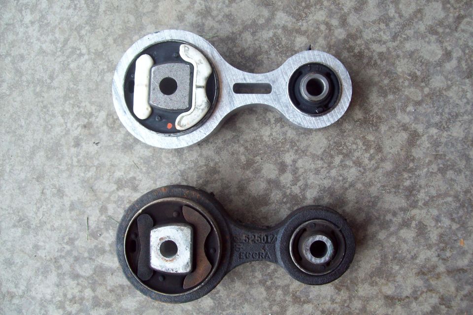 Two torque strut engine mounts on concrete, one aluminum and one dark cast metal