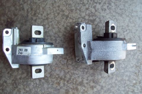 2006 Ford Fusion - Two metal engine/transmission mounts sit side by side on a concrete floor; the left one has a rubber isolator and a white label reading '29…