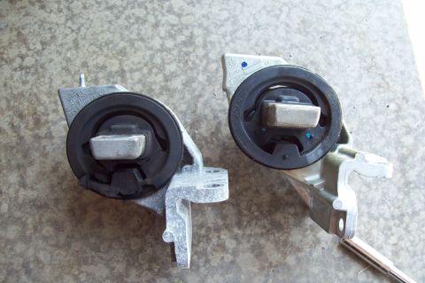 2006 Ford Fusion - Two engine/transmission mounts shown side by side on a concrete floor, each with a black rubber isolator, chromed steel weight, and cast al…