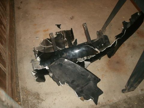 1998 Lincoln Mark VIII - Damaged black car bumper lies on a concrete floor, with visible cracks and torn pieces.