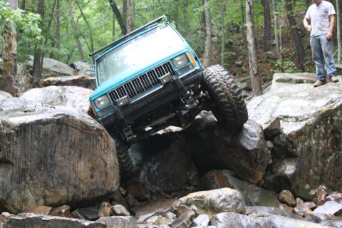 1984 Ford Bronco II - Jeep Cherokee XJ tackles a difficult rock crawling obstacle in a wooded area.