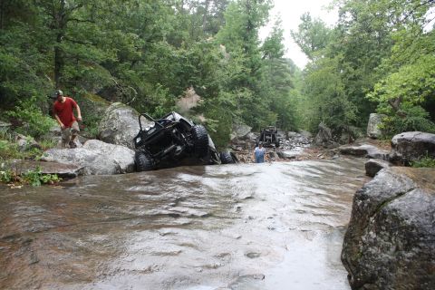1984 Ford Bronco II - Off-road vehicles traverse a challenging rocky stream, with one vehicle appearing stuck.