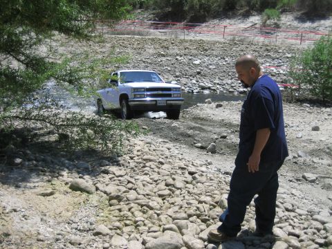 1986 Ford Bronco - A white 1995 Chevrolet C/K pickup truck navigates a rocky stream bed, with a man standing nearby.