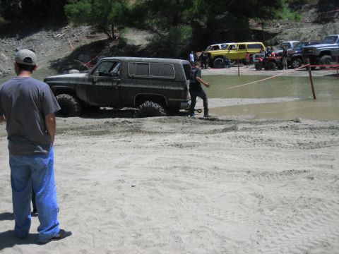 1986 Ford Bronco - Several off-road vehicles are gathered near a muddy water area, with one SUV deeply stuck in the sand.