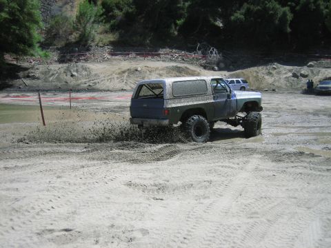 1986 Ford Bronco - Off-road vehicle navigates a muddy terrain, with another vehicle in the distance.