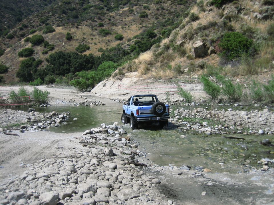 Blue convertible SUV with spare tire on rear, driving through a rocky stream bed