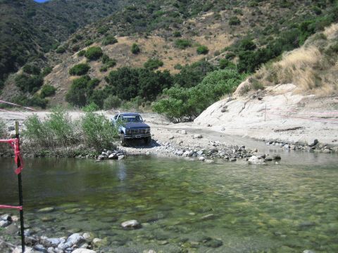 1986 Ford Bronco - Ford Bronco navigates a rocky stream in a dry, hilly landscape.