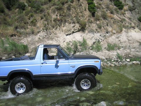 1986 Ford Bronco - A blue 1986 Ford Bronco navigates a rocky stream bed.