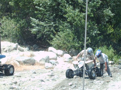 1986 Ford Bronco - Two individuals are interacting with a four-wheeled all-terrain vehicle in a natural, outdoor setting.