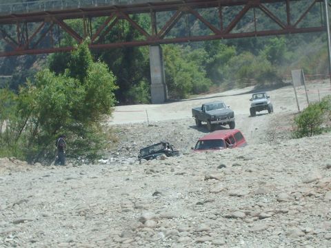1986 Ford Bronco - Off-road vehicles traverse a challenging rocky terrain beneath a large bridge structure.