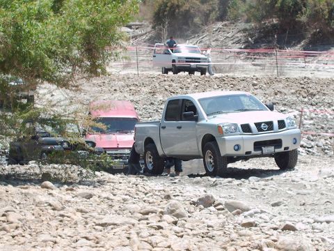 1986 Ford Bronco - Several vehicles are navigating a rocky, off-road terrain with trees and dry brush visible.