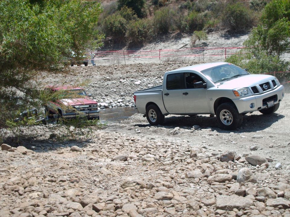 Silver Nissan Titan pickup truck and red Chevrolet C/K pickup truck crossing a rocky stream