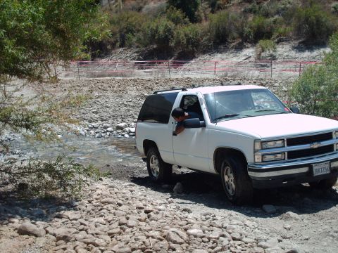1986 Ford Bronco - This white SUV is navigating a dry creek bed with rocky terrain and sparse vegetation.
