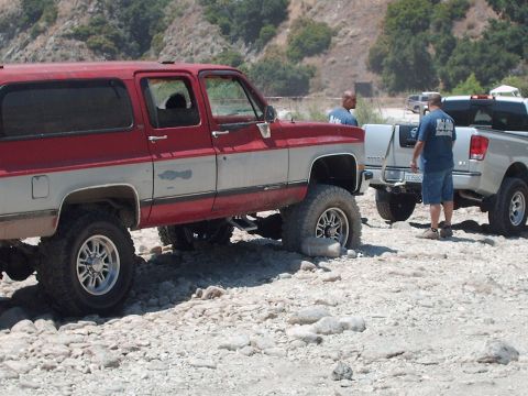 1986 Ford Bronco - This lifted, two-tone SUV is parked on a rocky surface next to another pickup truck.