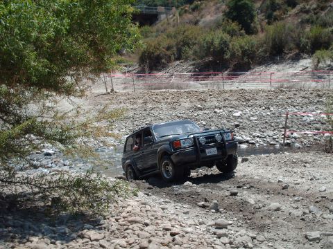 1986 Ford Bronco - A dark SUV navigates a challenging off-road terrain with a rocky stream bed.