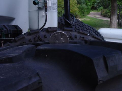 1979 Ford Bronco - Tire tread detail with a quarter for scale. Propane tank in background.