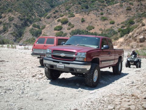 1986 Ford Bronco - Two trucks and an ATV are parked in a dry riverbed with mountainous terrain behind them.