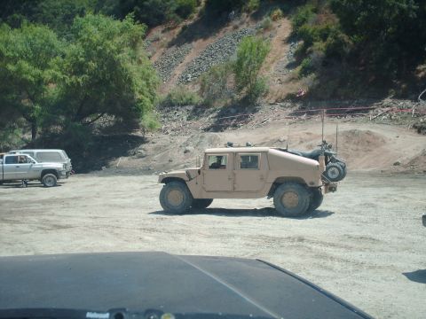 1986 Ford Bronco - A tan military-style SUV is parked in an outdoor lot with other vehicles visible in the background.