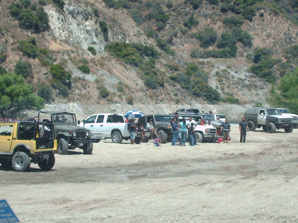 Several off-road vehicles parked on a dirt surface with a rocky hillside in the background