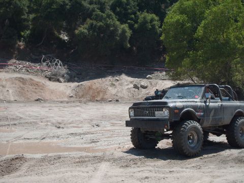 1986 Ford Bronco - This modified truck is seen off-road with a wooded hillside in the background.