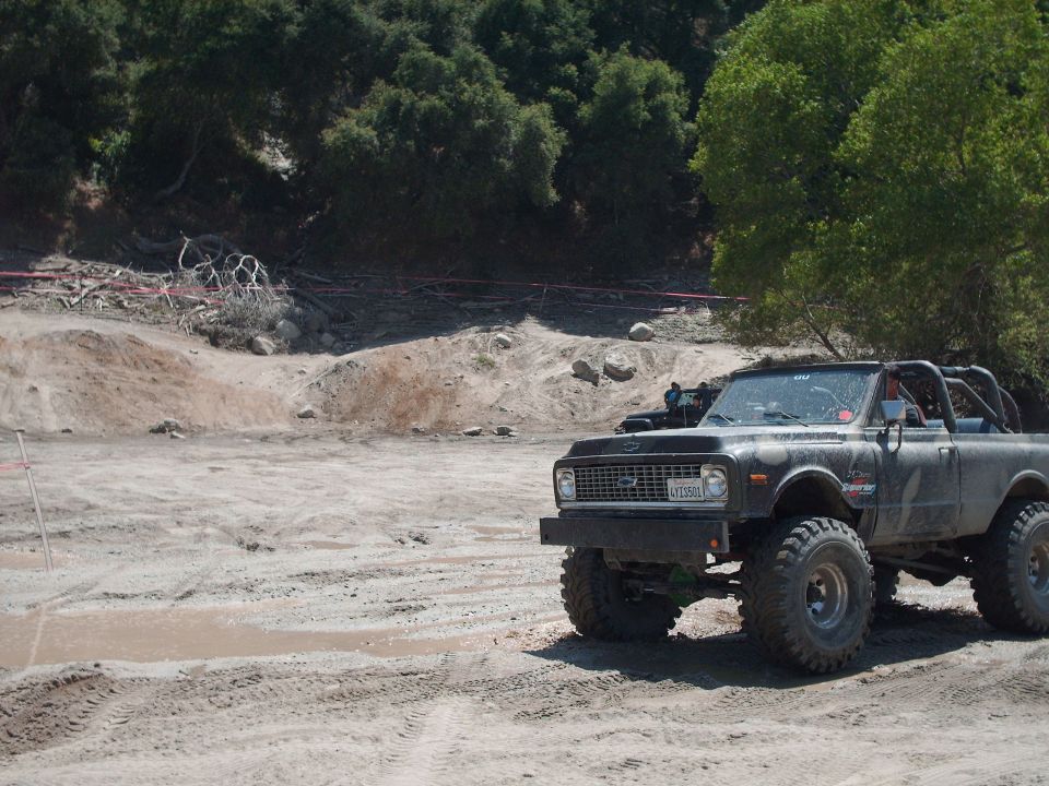 Black off-road truck with large tires and roll cage parked on dirt