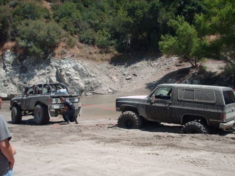1986 Ford Bronco - Two off-road vehicles are stuck in the mud, with one attempting to pull the other out.