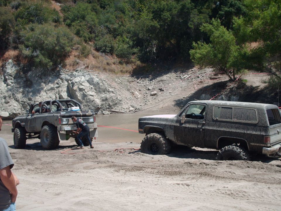 Two off-road vehicles stuck in mud, one being winched by the other