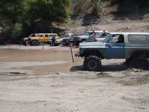 1986 Ford Bronco - Several off-road vehicles are gathered in a muddy area, with one vehicle partially submerged.