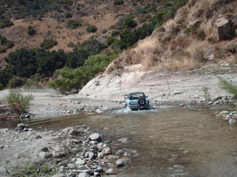 1986 Ford Bronco - A light blue 1986 Ford Bronco navigates a water crossing on a dusty trail.
