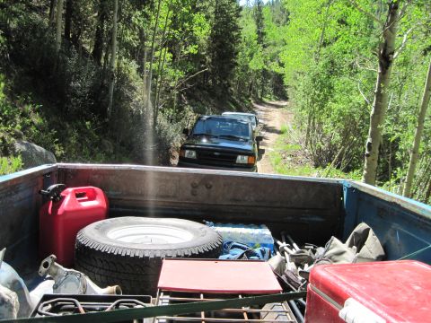 1978 Ford F-150 - Two vehicles travel on a dirt road through a forest, viewed from the bed of a pickup truck.