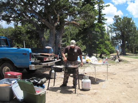1978 Ford F-150 - A blue Ford pickup truck is parked at a campsite while a man cooks food on a grill.