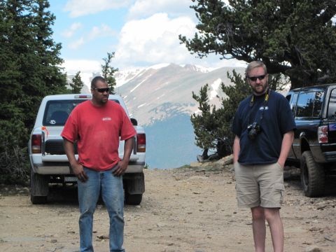 1978 Ford F-150 - Two men stand beside pickup trucks on a mountain road with a scenic view.