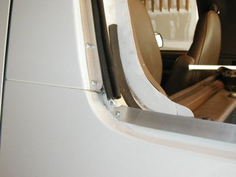 1995 Ford Bronco - Close-up of the interior of a white vehicle, focusing on the door frame and brown seats, possibly during a soft top installation.