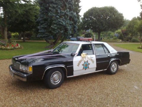 1991 Ford Crown Victoria - This police car, decorated with ribbons, is parked on a gravel driveway in front of a lawn and trees.