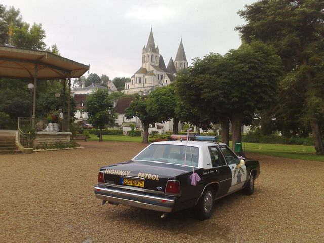Black and white police car, rear 3/4 view, parked on gravel with a church in the background