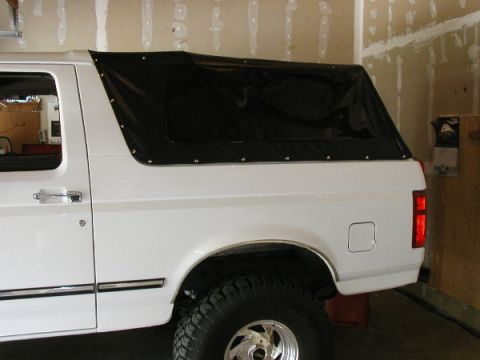 1995 Ford Bronco - A white Ford Bronco is shown from the side with a black soft top installed.