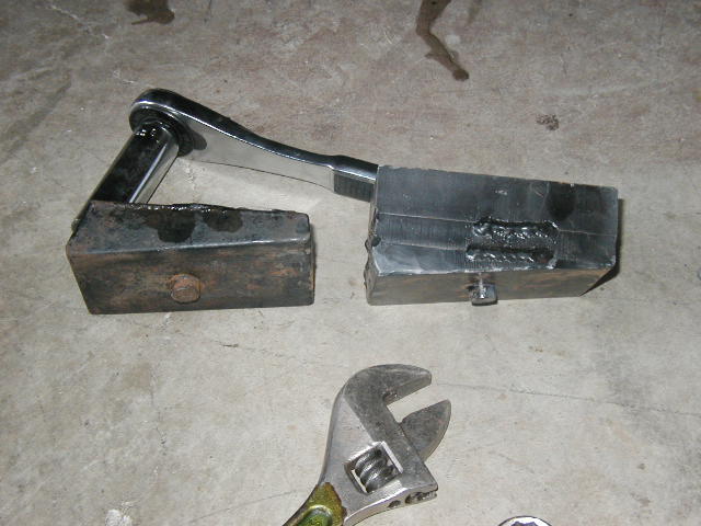 Two welded steel blocks joined by a chrome lever, with a crescent wrench nearby on concrete