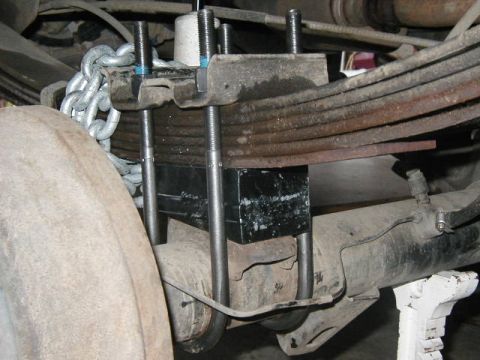 1995 Ford Bronco - Close-up view of aftermarket lift blocks and a chain installed on a vehicle's rear axle and leaf springs.