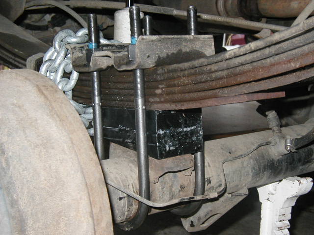 Leaf spring and axle U-bolt assembly under a truck with chain and tire visible